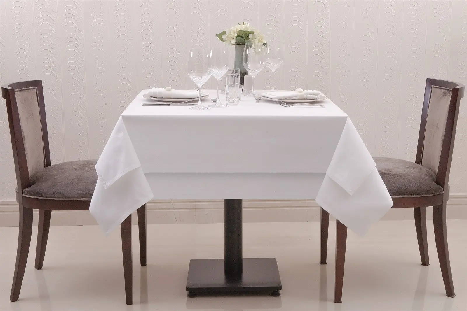 İki kişilik kare restoran masasında beyaz masa örtüsü ve geniş kapak