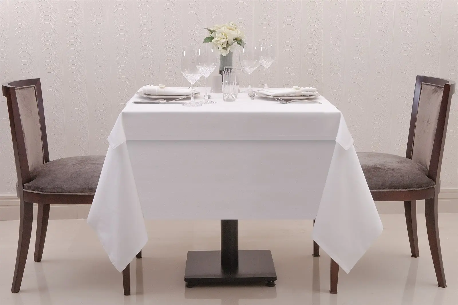 İki kişilik kare restoran masasında uzun sarkan beyaz masa örtüsü ve kapak